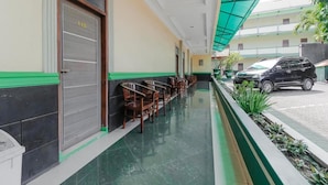 A hotel corridor with a green-tiled floor, wooden chairs along the wall, and a closed door with a number plate. - Permata Hijau (North Cirebon)