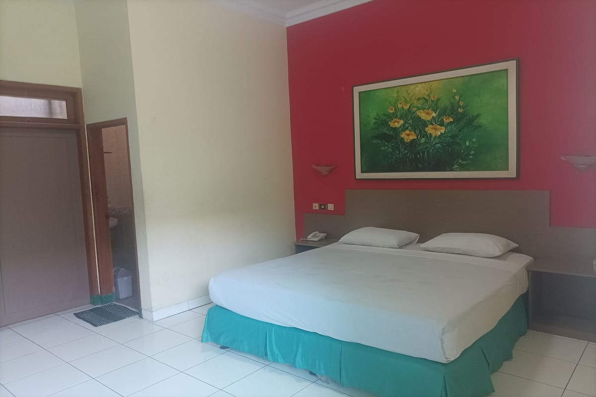 Une chambre d’hôtel avec un lit, un mur rouge, une porte verte et un tableau représentant des fleurs.