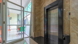 A modern elevator with a digital display, a glass door entrance, and a view of an outdoor seating area. - Permata Hijau (North Cirebon)
