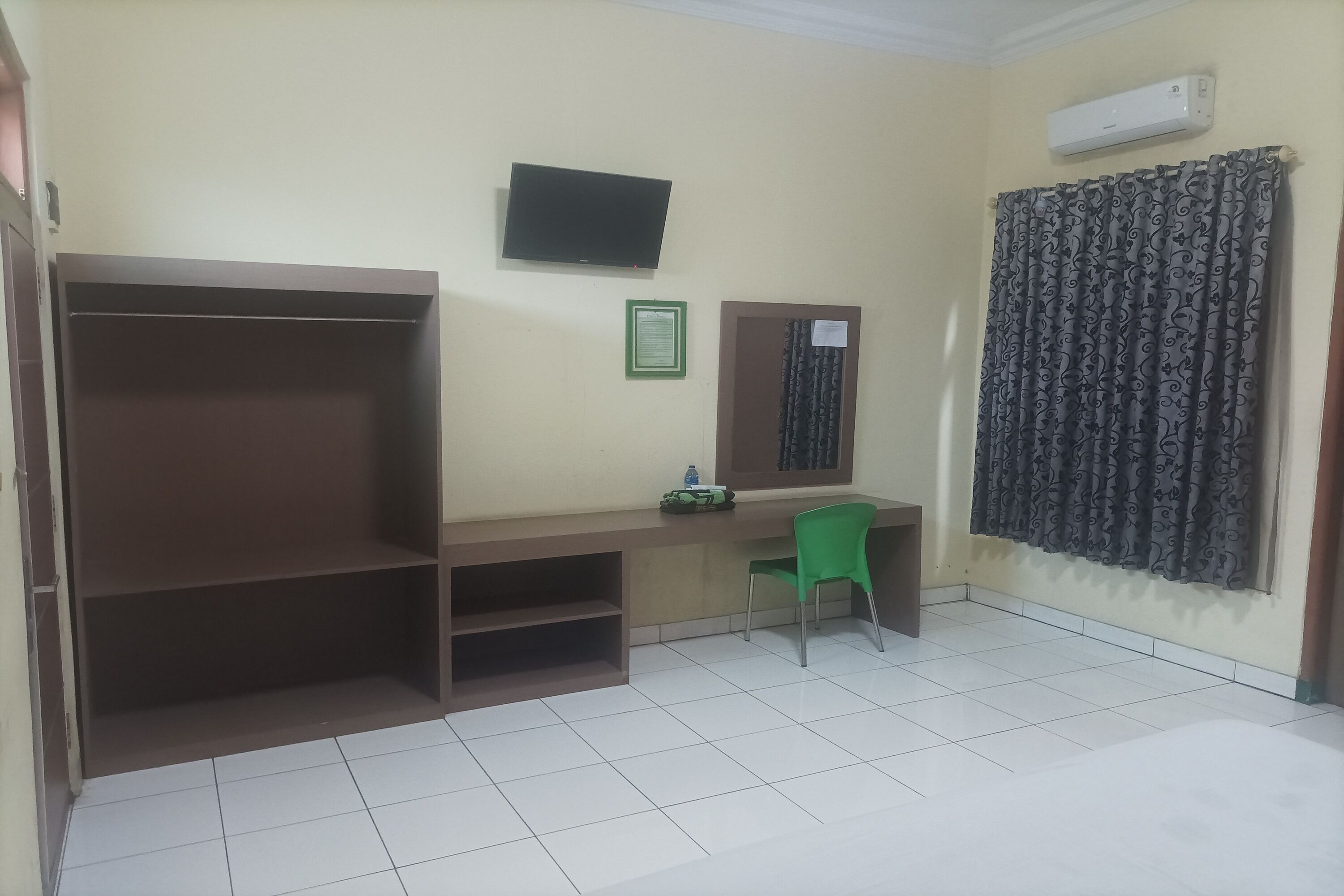 A room with a desk, a chair, a television, a shelf, and a curtain.