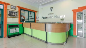 A hotel reception area with a green and orange color scheme, a reception desk, framed pictures on the wall, and a sign that reads "HOTEL PERNIITA HIAU". - Permata Hijau (North Cirebon)