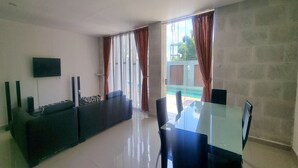 A modern living room with a glass dining table, black chairs, a sofa, and a TV mounted on the wall. - Tresna Villa 7 (Nusa Dua)