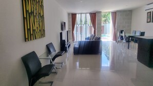 A modern hotel lobby with a seating area, a reception desk, and a large window with curtains. - Tresna Villa 7 (Nusa Dua)