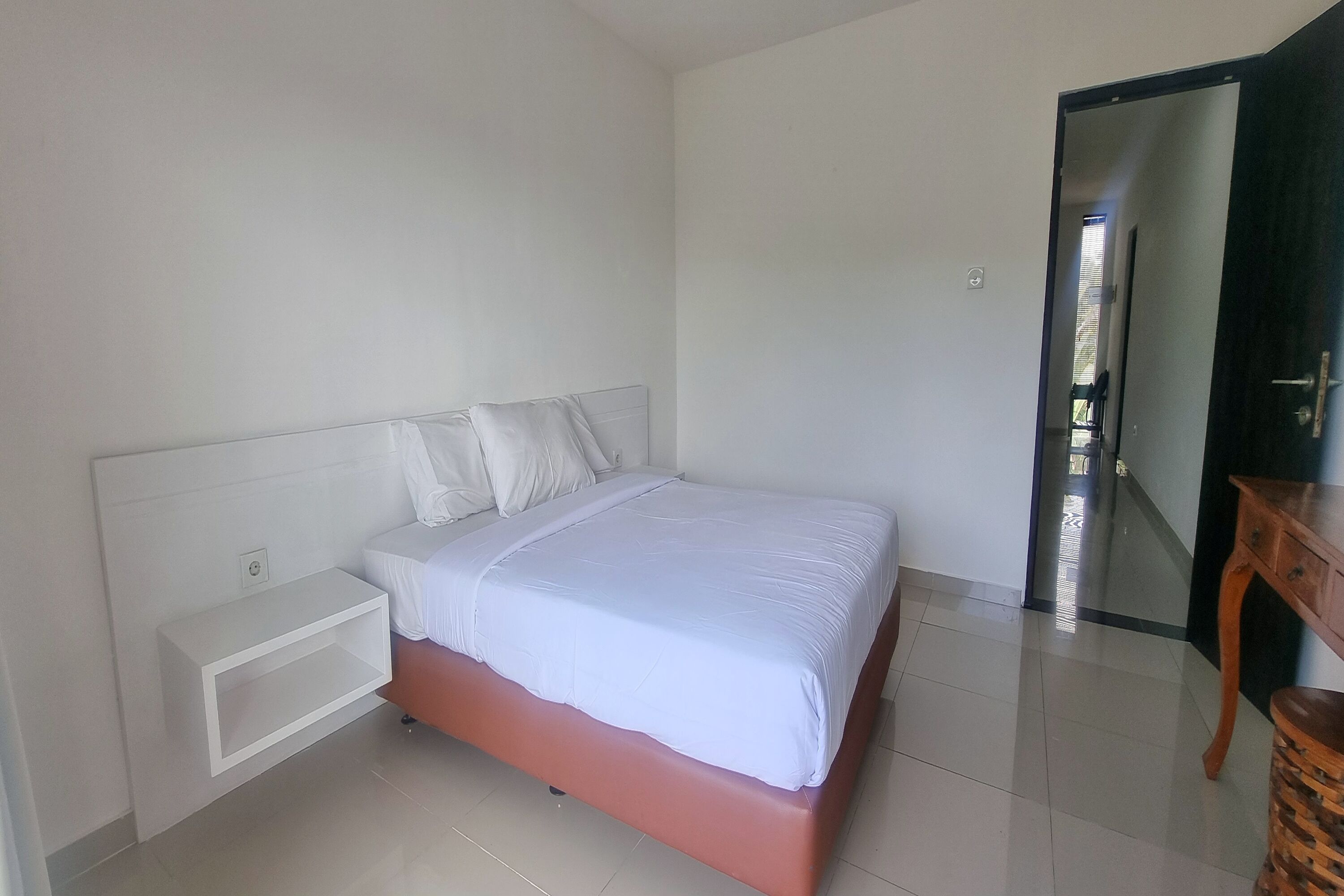 A bedroom with a bed, a nightstand, a wooden side table, and a door leading to another room.