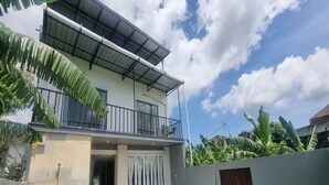 A two-story house with a balcony, a covered outdoor area, and a pair of blue lounge chairs. - Tresna Villa 7 (Nusa Dua)
