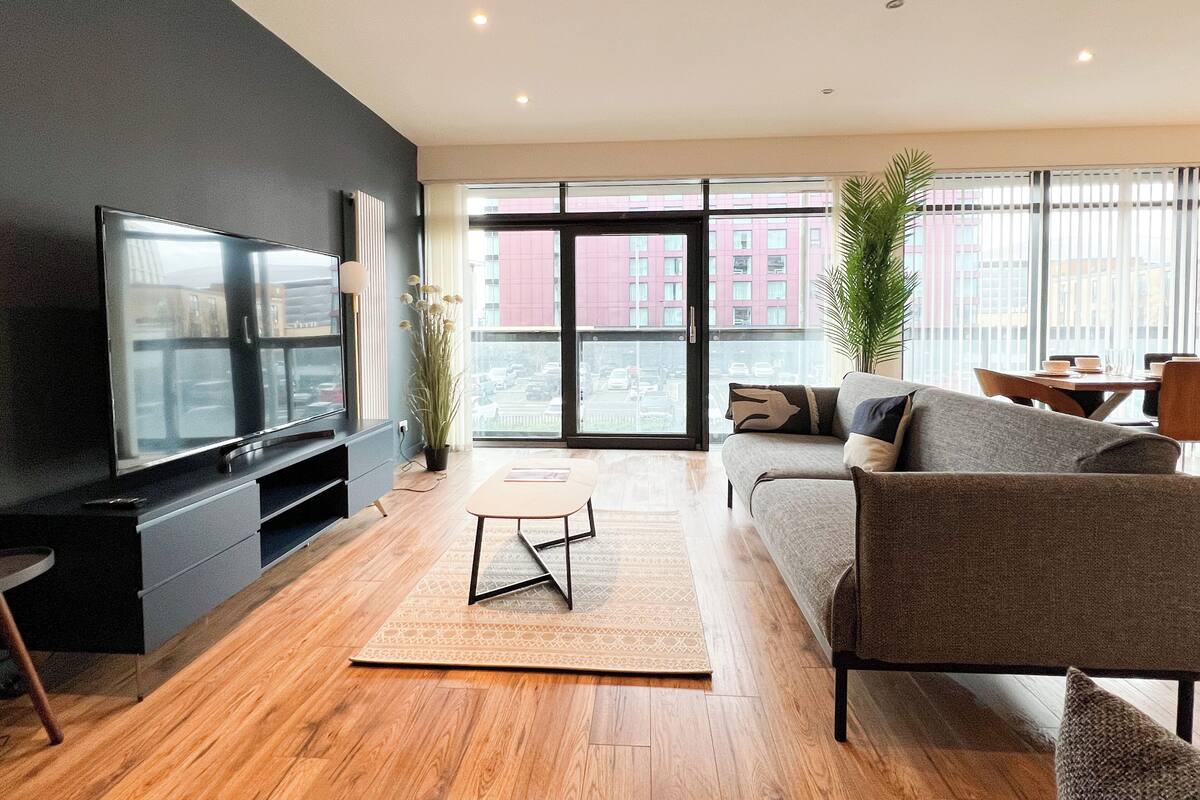 A modern living room with a flat-screen TV, a sofa, a dining table, and a large window with a city view.