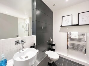 Ein modernes Badezimmer mit einem weißen Waschbecken, einer Toilette und einer Dusche. An den Wänden befinden sich gerahmte Bilder und ein Handtuchhalter.