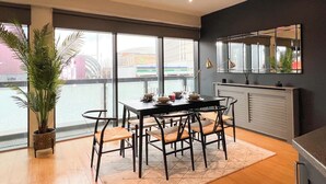 A modern dining area with a table set for four, surrounded by chairs, a large potted plant, and a view of the street outside. - Hydro Apartments (Glasgow)