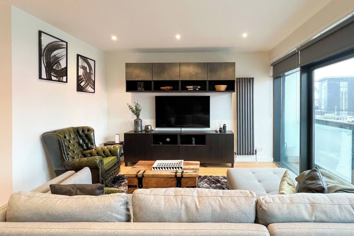 A modern living room with a large flat-screen TV, a leather armchair, a sofa, and a coffee table.