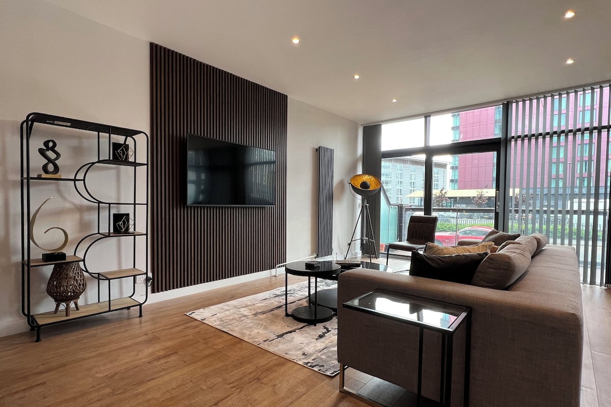 A modern living room with a sofa, a TV mounted on a wall, a floor lamp, and a bookshelf.