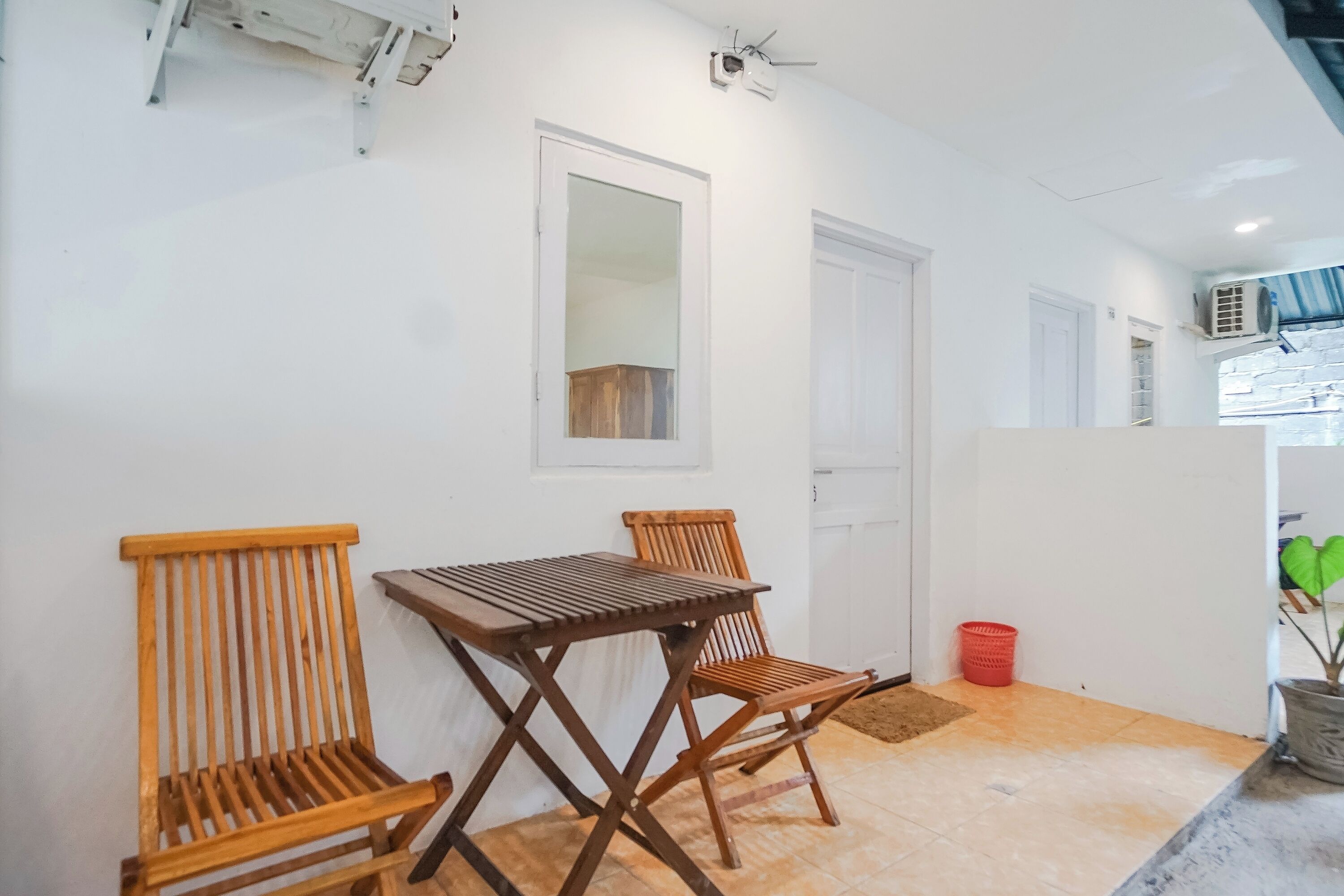 A room with a wooden table and two chairs, a white door, and a window with a view of a building outside.