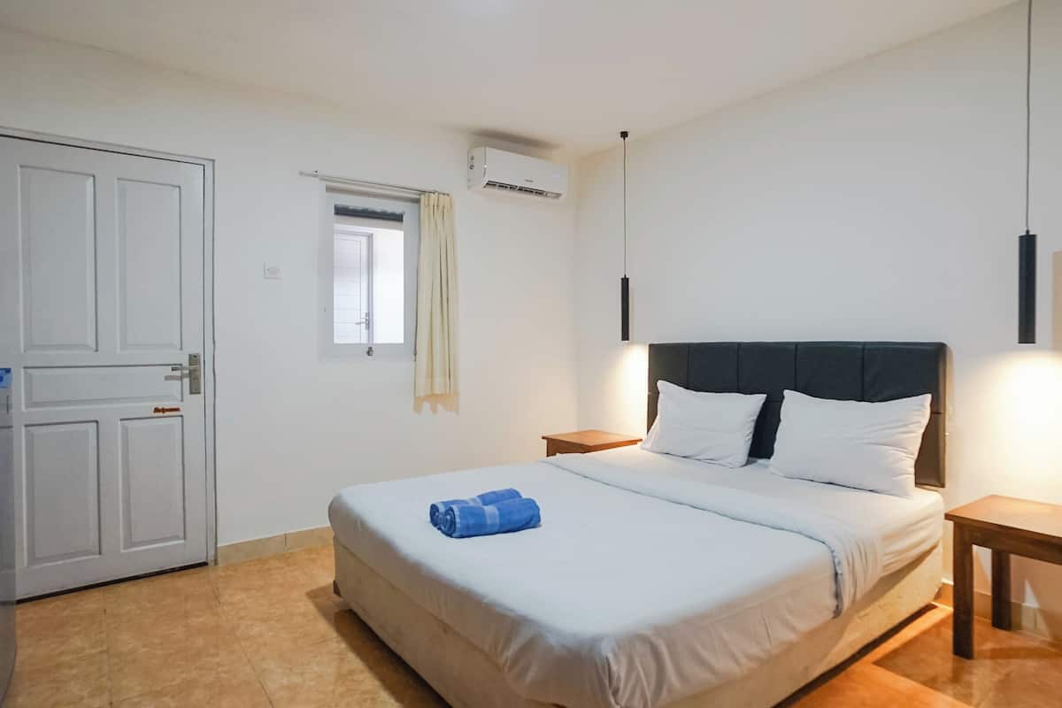 A bedroom with a bed, a nightstand, a window with curtains, an air conditioning unit, and a door.