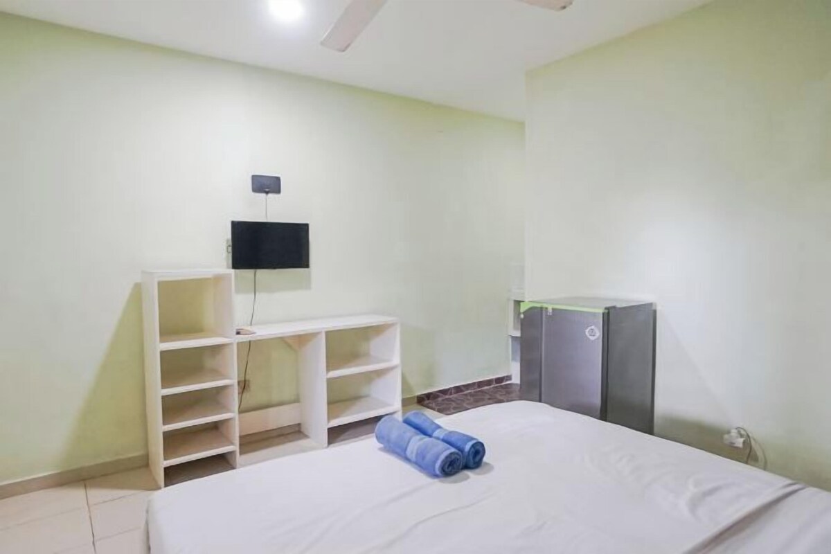 A hotel room with a bed, a TV mounted on the wall, a desk with shelves, and a refrigerator.