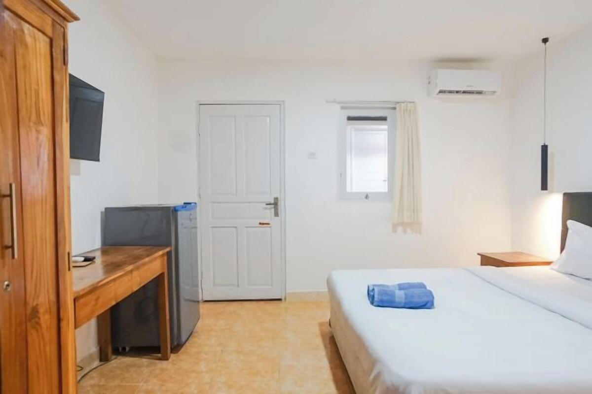 A hotel room with a bed, a desk, a television, and an air conditioning unit.
