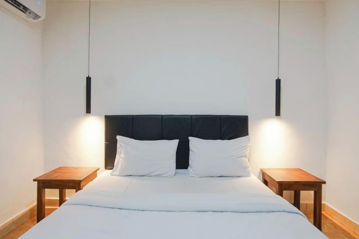 A neatly made bed with white linens and two pillows, flanked by two wooden nightstands.