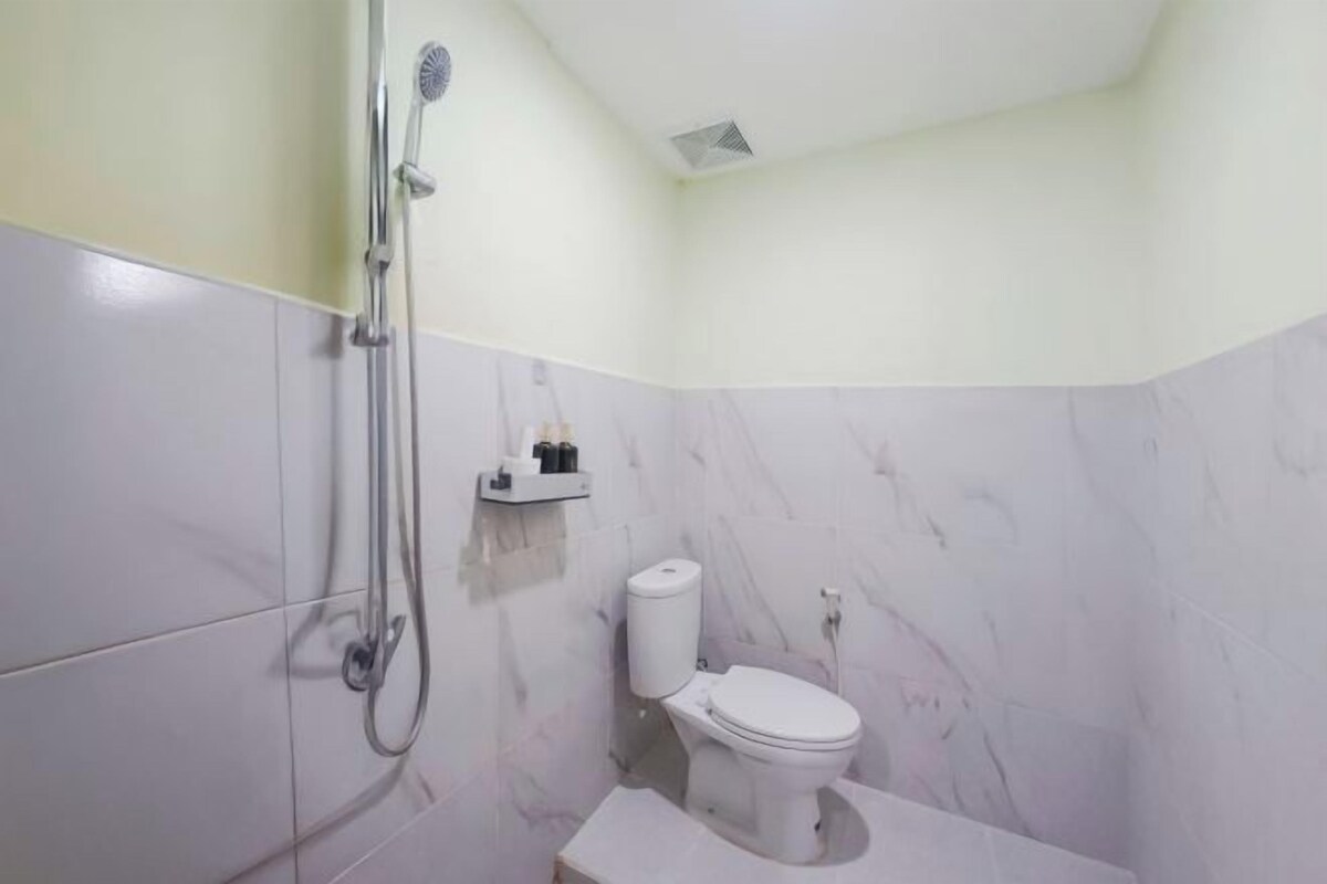 A small bathroom with a toilet, a shower, and a marble wall.