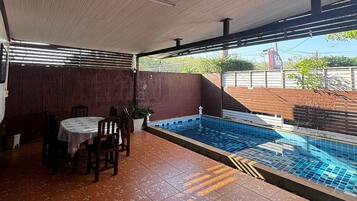 A covered outdoor area with a pool, a dining table with chairs, and a view of the surrounding area.