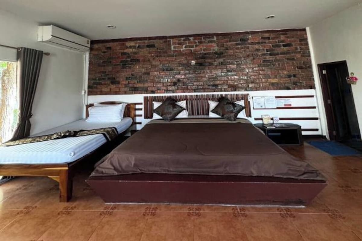Un dormitorio con una cama grande, una cama más pequeña, una pared de ladrillo, un cabecero de madera y una mesita de noche.