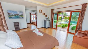 Habitación de hotel con una cama grande, un escritorio, una silla y vista a un jardín a través de un ventanal corredero.