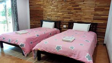Dos camas individuales con ropa de cama rosa y almohadas blancas, cabeceras de madera y una pared de madera con una lámpara.