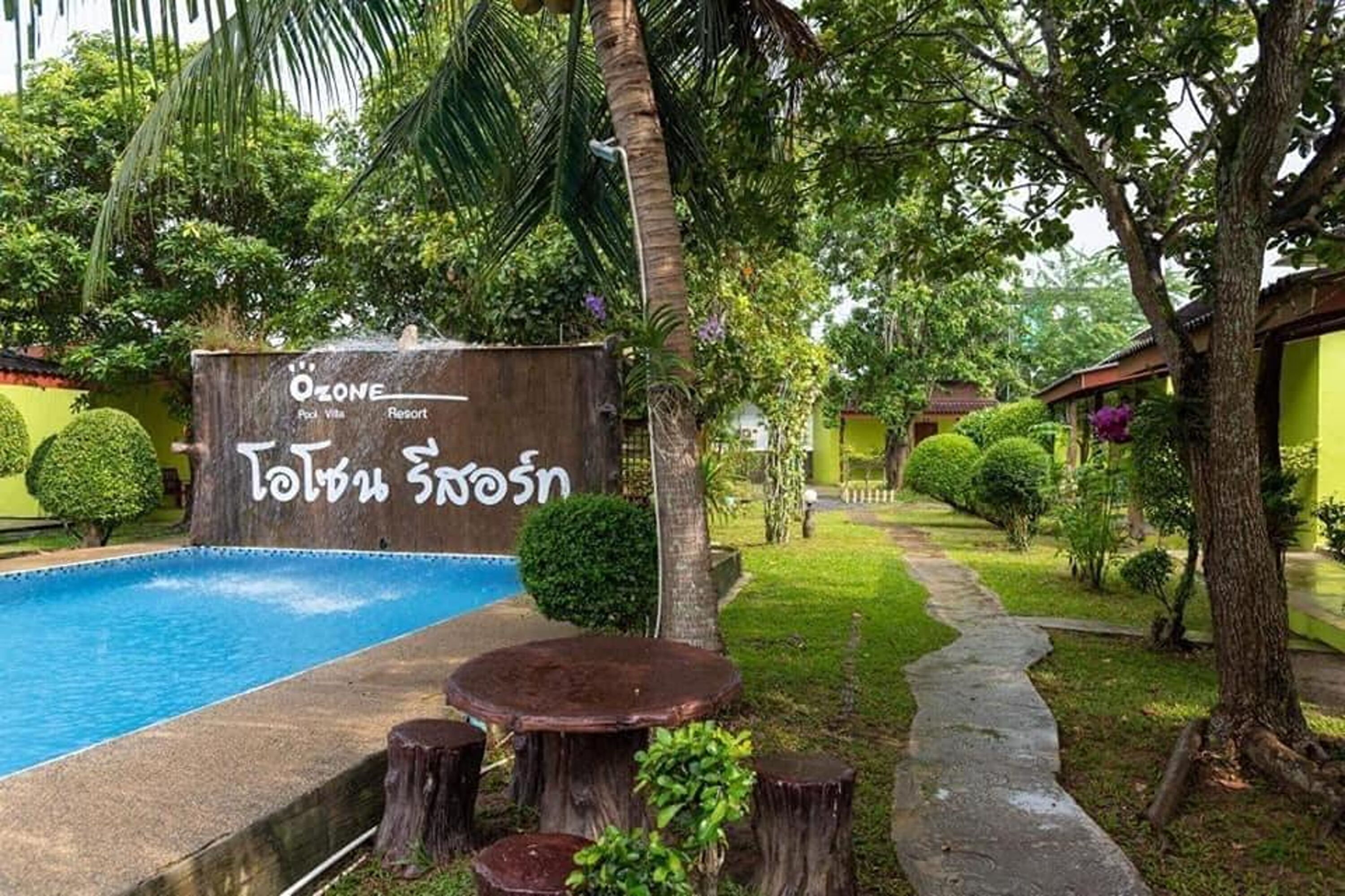 Un resort con piscina, un cartel con texto y abundante vegetación.