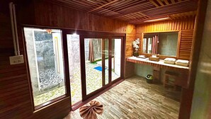 Un interior de madera con un divisor corredizo de vidrio que da a un balcón, una pequeña zona de estar con un espejo y suelo de baldosas.
