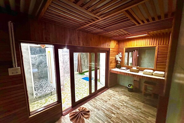 A wooden interior with a sliding glass door leading to a balcony, a small seating area with a mirror, and a tiled floor.