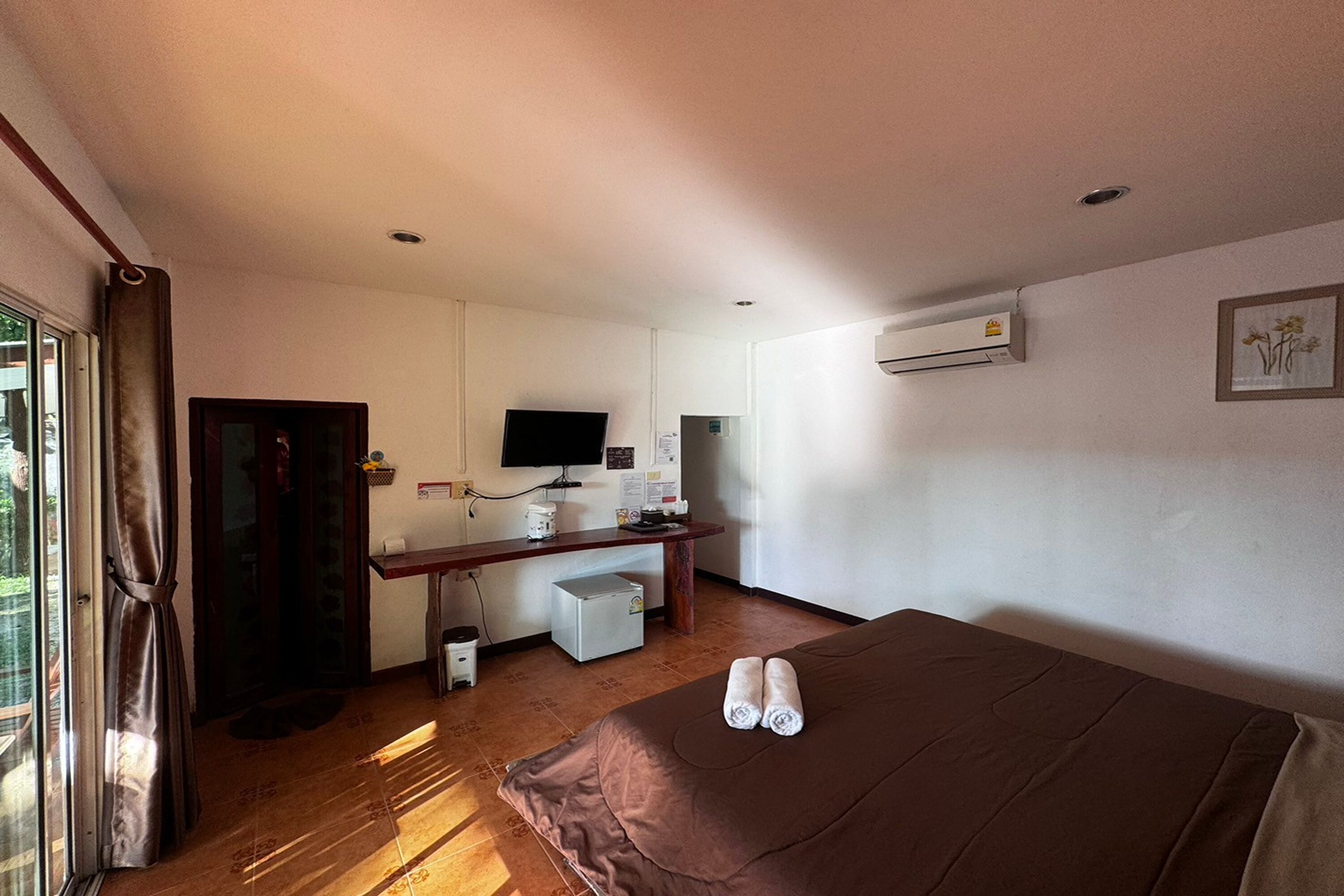 A hotel room with a bed, a desk with a computer, a small refrigerator, and a TV.