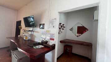 Une petite cuisine équipée d’un réfrigérateur, d’un four à micro-ondes et d’une machine à café. Un téléviseur à écran plat est fixé au mur, et il y a un petit tabouret en bois.