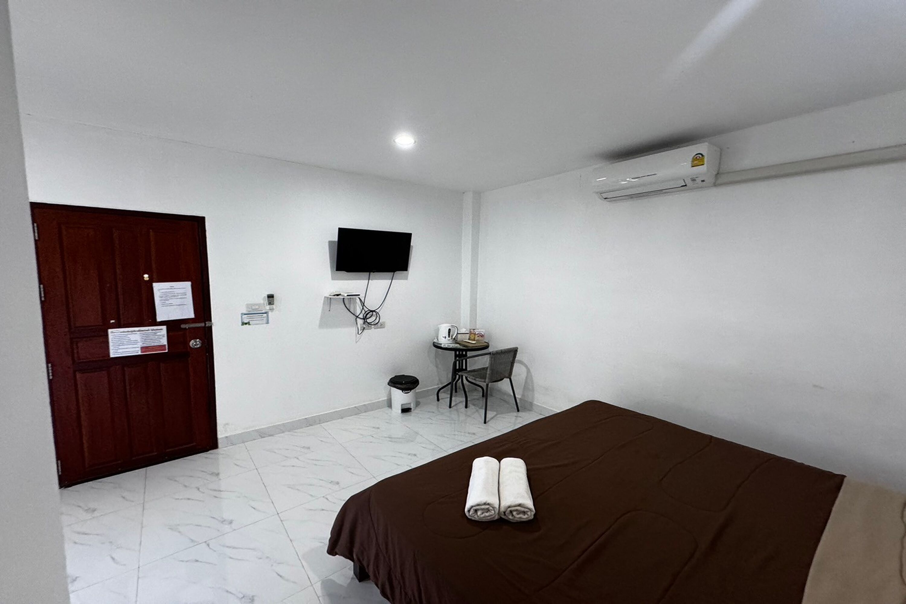 A hotel room with a bed, a desk, a chair, a TV, and an air conditioning unit.