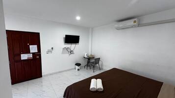 A hotel room with a bed, a desk, a chair, a TV, and an air conditioning unit.