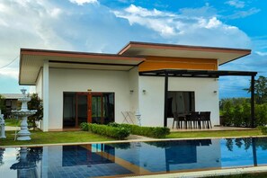 Uma casa moderna com piscina, varanda coberta e jardim com fonte.