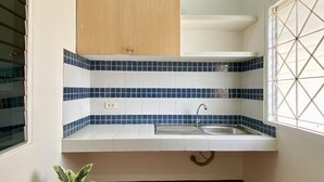 A small kitchen with a sink, blue and white tiles, a wooden cabinet, and a potted plant. - Andaman Residence (Thep Krasattri)