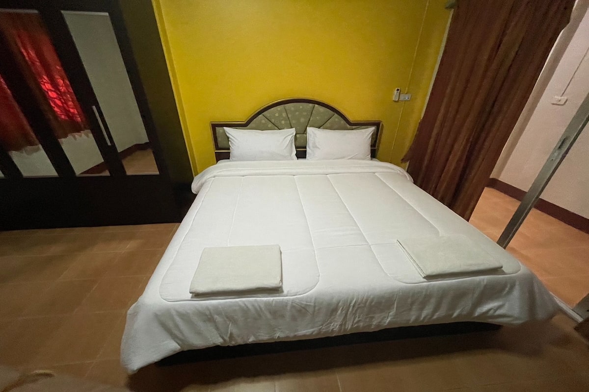 Una cama bien hecha con sábanas y almohadas blancas, un cabecero de madera y una pared amarilla.