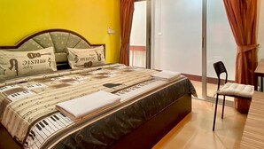 A bedroom with a bed, pillows, a chair, and a sliding glass door leading to a balcony. - Andaman Residence (Thep Krasattri)