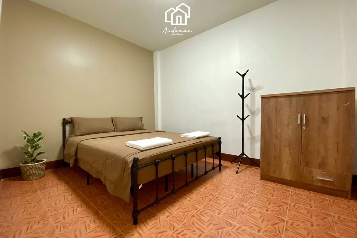 Un dormitorio con cama, armario, lámpara de pie y planta en maceta.