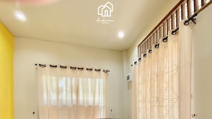 A living room with a purple sectional sofa, a flat-screen TV, and a window with curtains. - Andaman Residence (Thep Krasattri)