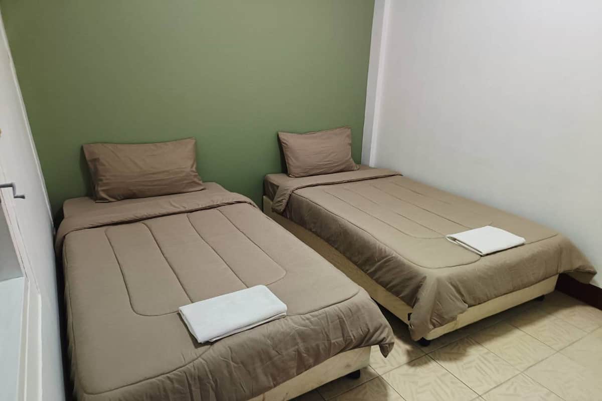 Dos camas individuales con ropa de cama color beige en una habitación con paredes verdes y blancas.