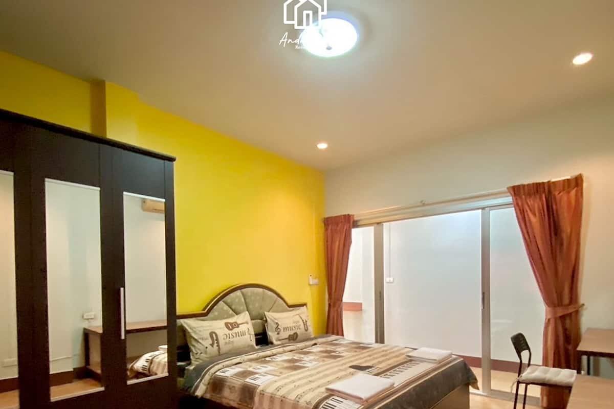 Un dormitorio con cama, armario, escritorio y puerta corrediza de vidrio al exterior.