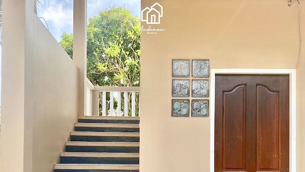 A staircase leading to a balcony with a railing, a wooden door, and a potted plant. - Andaman Residence (Thep Krasattri)