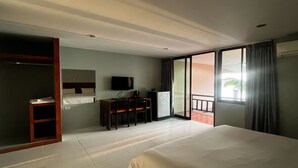 Een hotelkamer met een groot bed, een bureau met stoel, een televisie en een balkon met gordijnen.