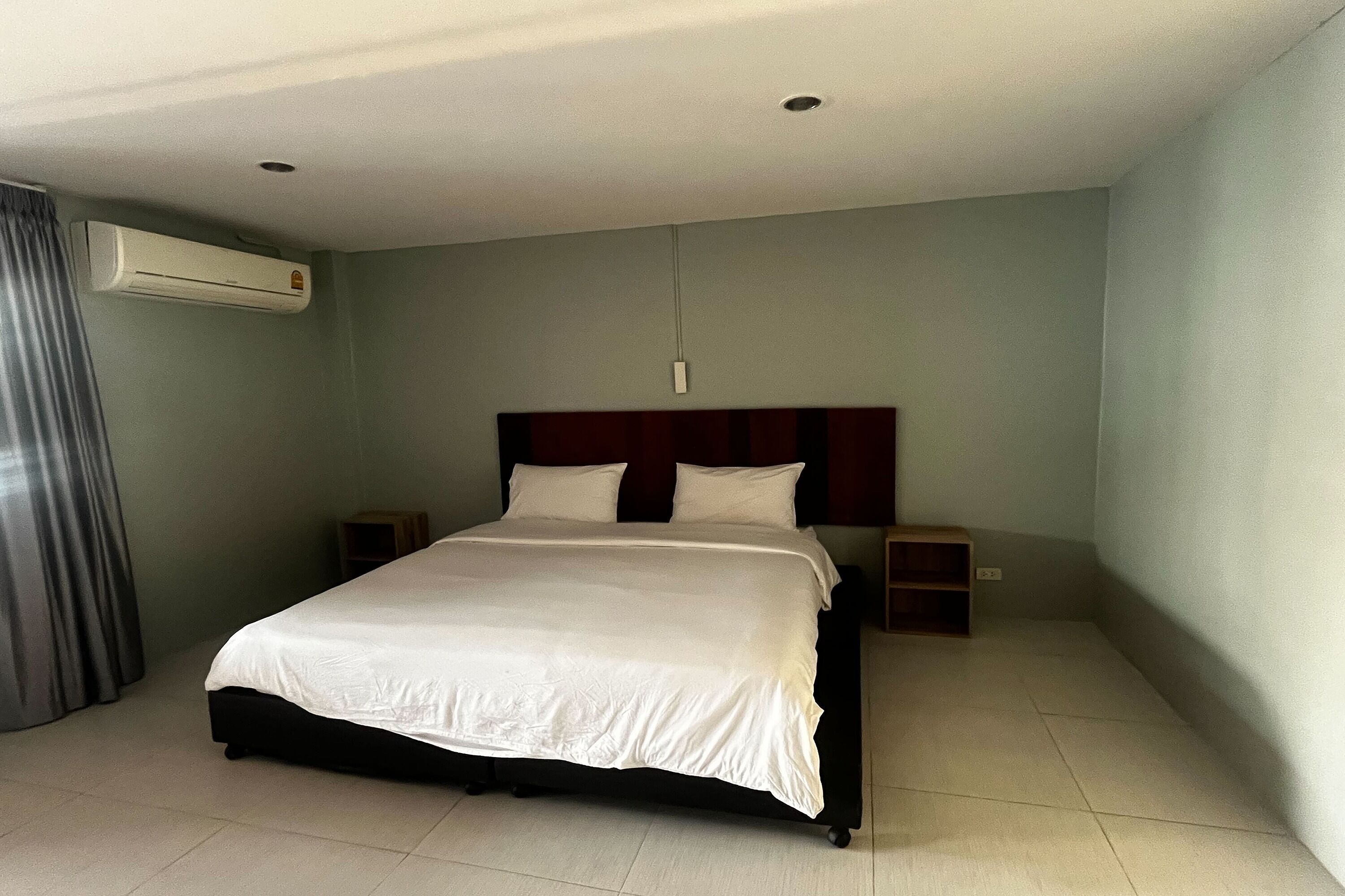A hotel room with a bed, a nightstand, an air conditioning unit, and a wall-mounted light fixture.