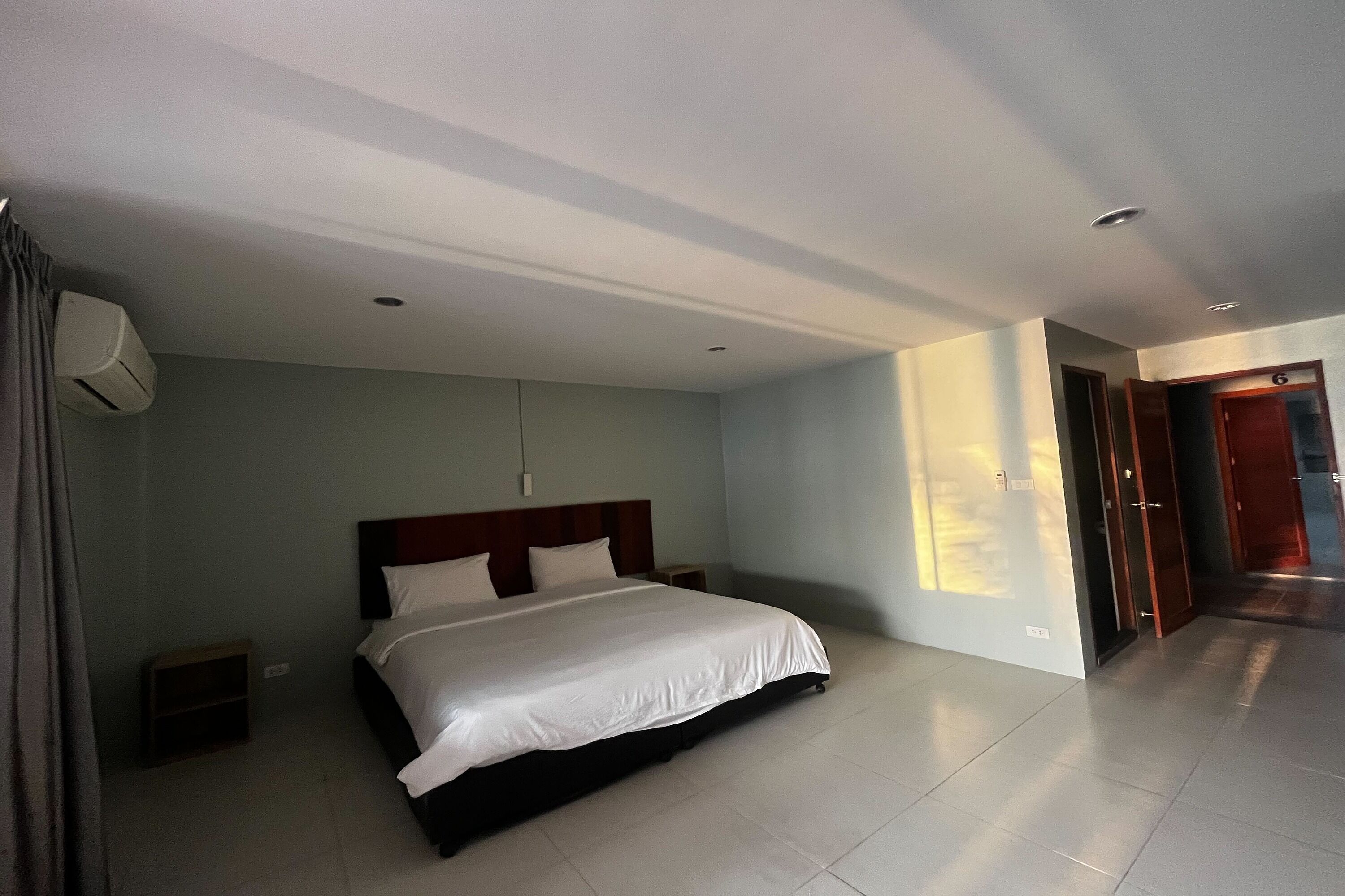 Habitación de hotel con una cama grande, una mesita de noche, aire acondicionado montado en la pared y una puerta que da a otra habitación.
