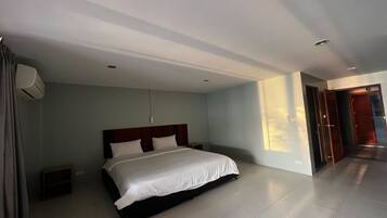 Habitación de hotel con una cama grande, una mesita de noche, aire acondicionado montado en la pared y una puerta que da a otra habitación.