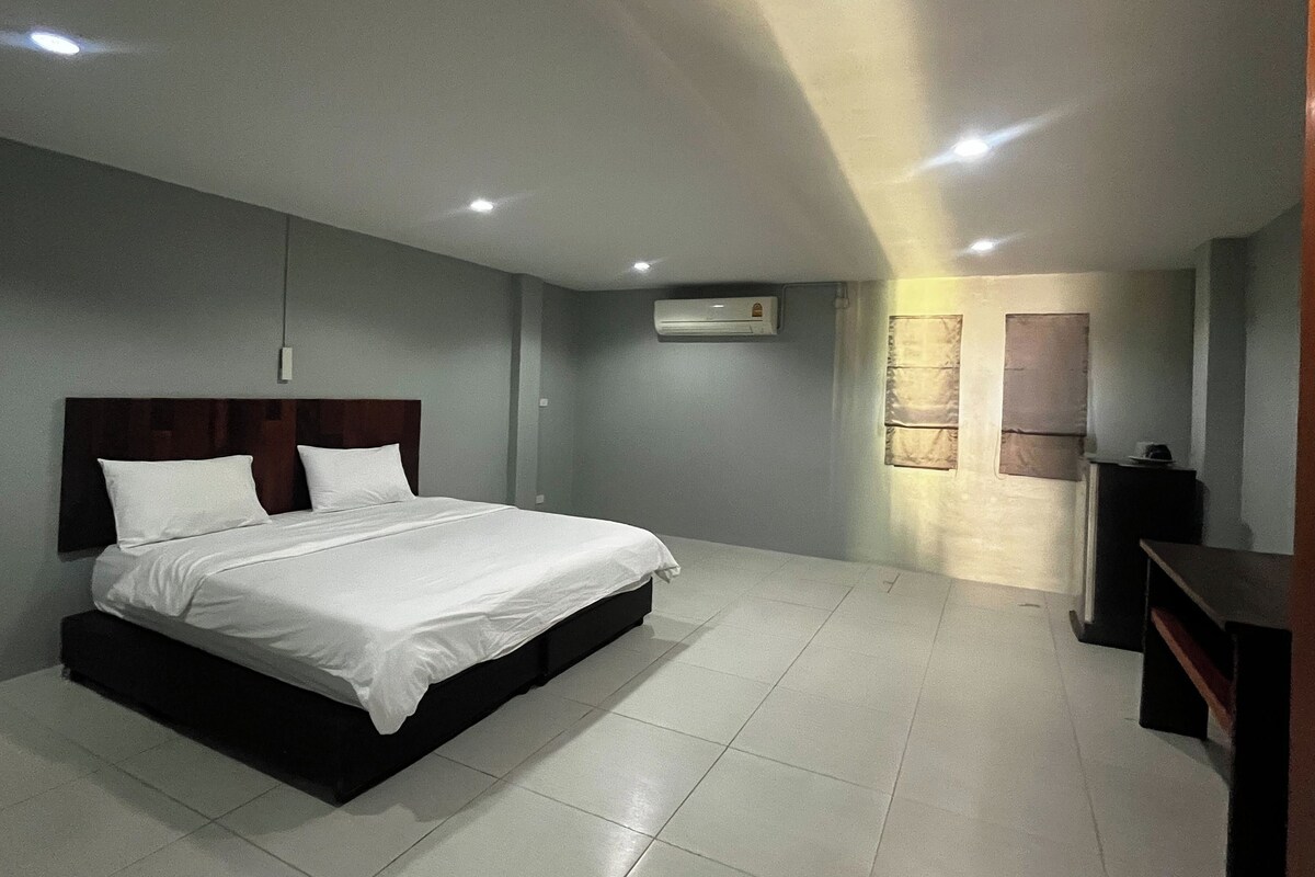 A hotel room with a bed, an air conditioning unit, a television, and a window with curtains.