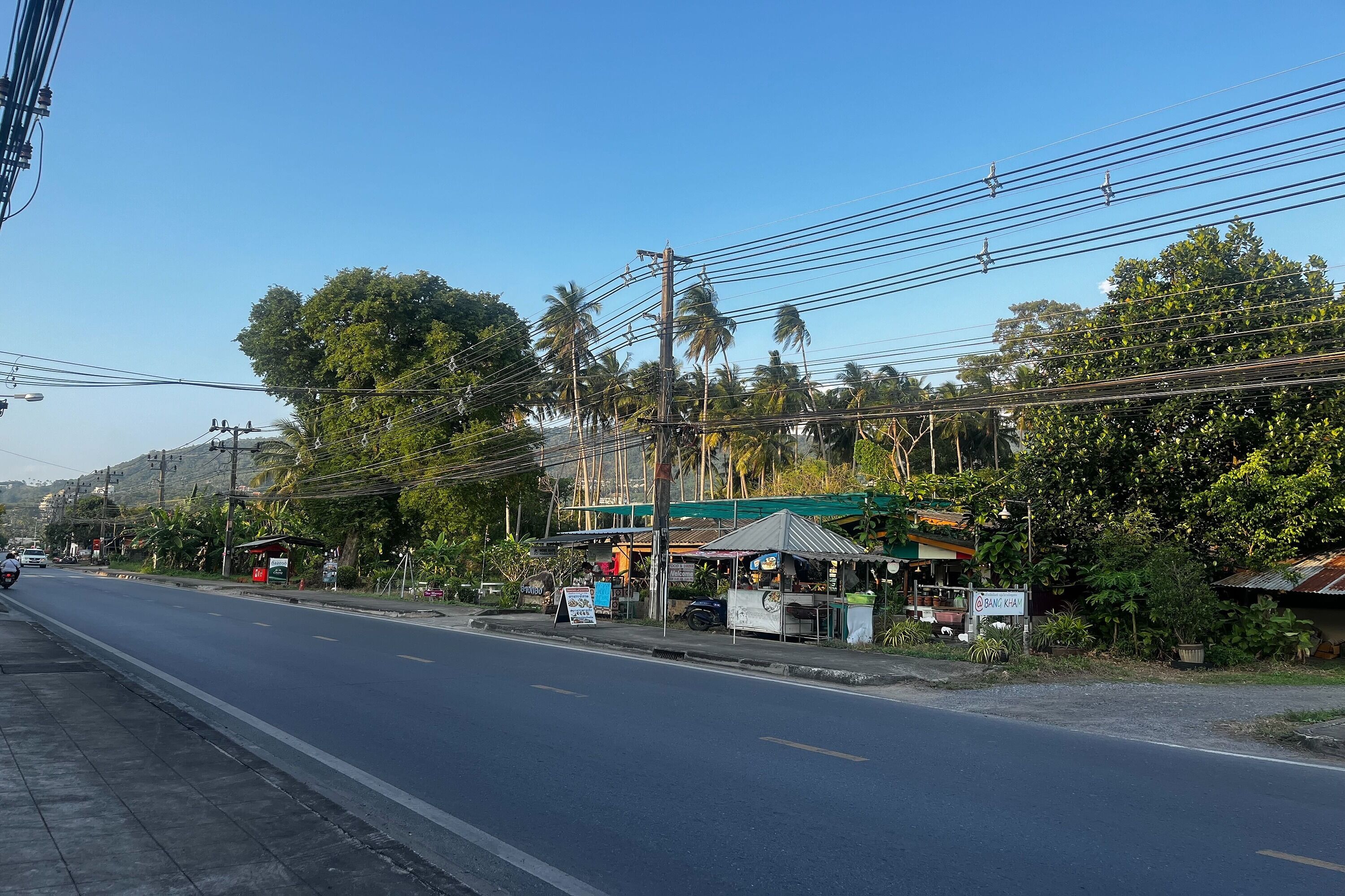 Une rue dégagée, avec des lignes électriques et une petite boutique au bord de la route, reconnaissable à son enseigne.