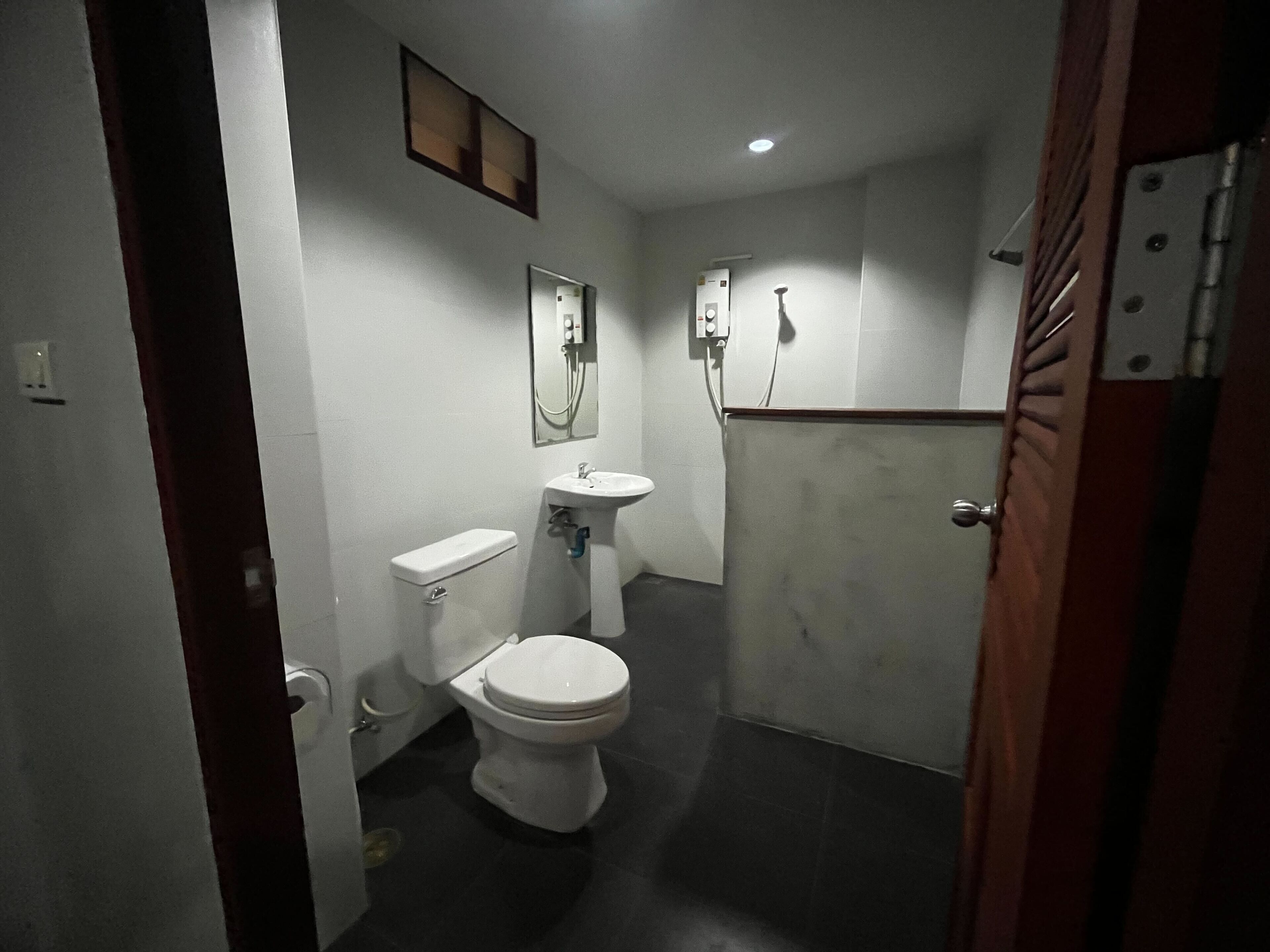 Une petite salle de bain étroite, équipée de toilettes, d’un lavabo et d’une douche.