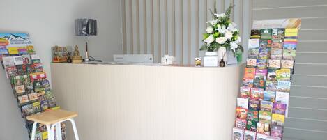A reception desk with a computer, a telephone, and a flower vase. There are posters and a chair to the left.