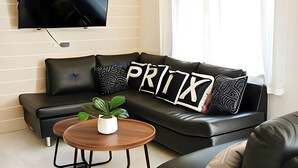 A modern living room with a black leather sofa, a flat-screen TV mounted on the wall, and a small wooden coffee table with a potted plant. - Prix Hotel (Chiang Mai)