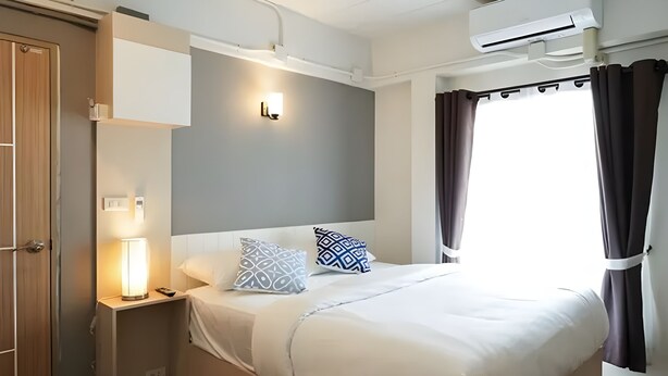 A hotel room with a bed, bedside lamp, air conditioning unit, and a window with curtains. - Prix Hotel (Chiang Mai)